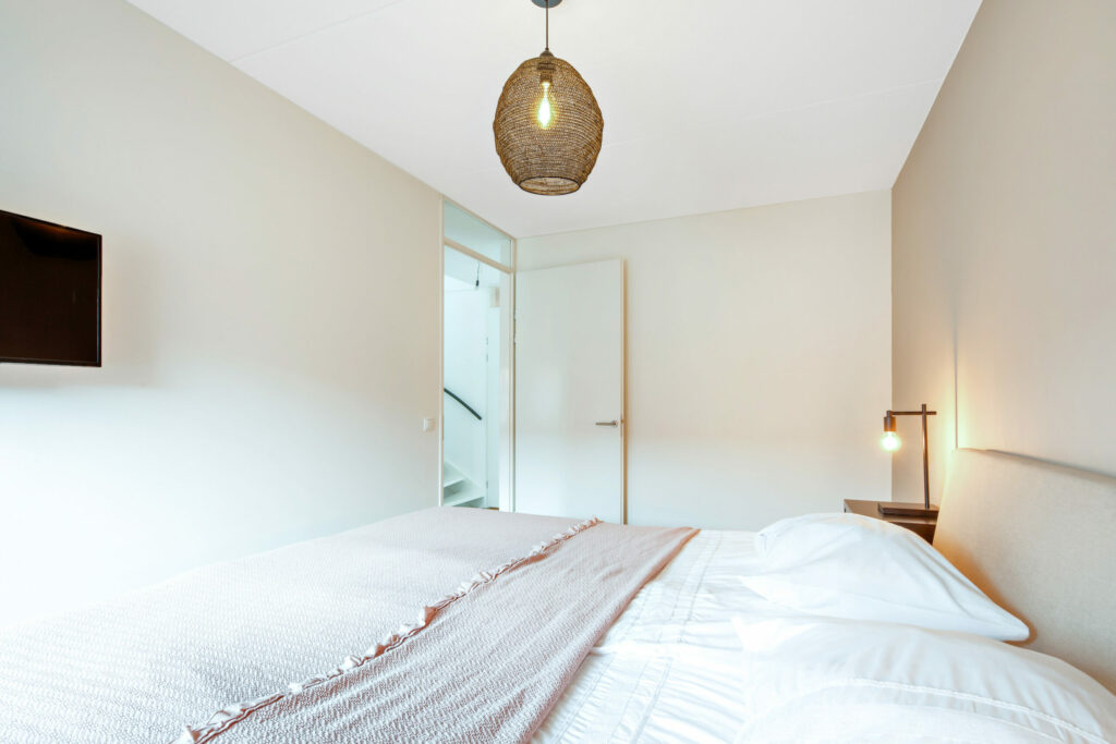Lichte slaapkamer met opgemaakt bed en hanglamp, vastgoedfoto