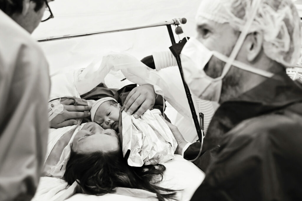 Moeder met pasgeboren baby op de borst omringd door zorgverleners