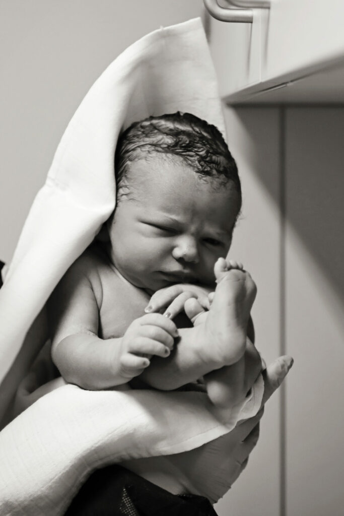 Zwart-witfoto van een pasgeboren baby in de handen van de verloskundige