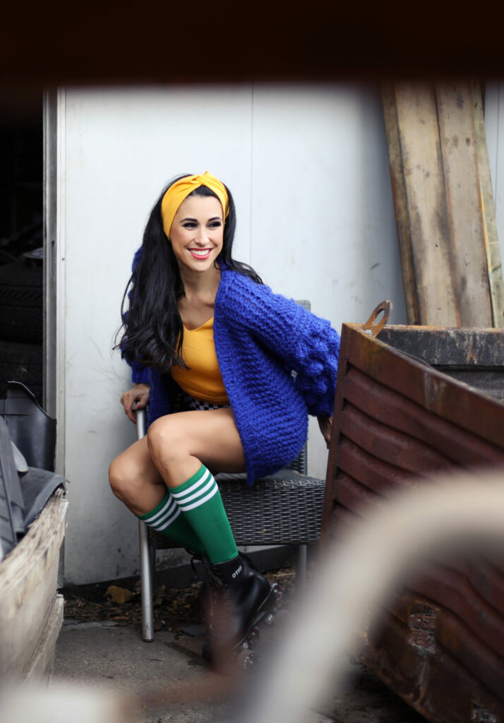 Vrouw in blauw vest zit op een stoel tussen oud ijzer, retro shoot