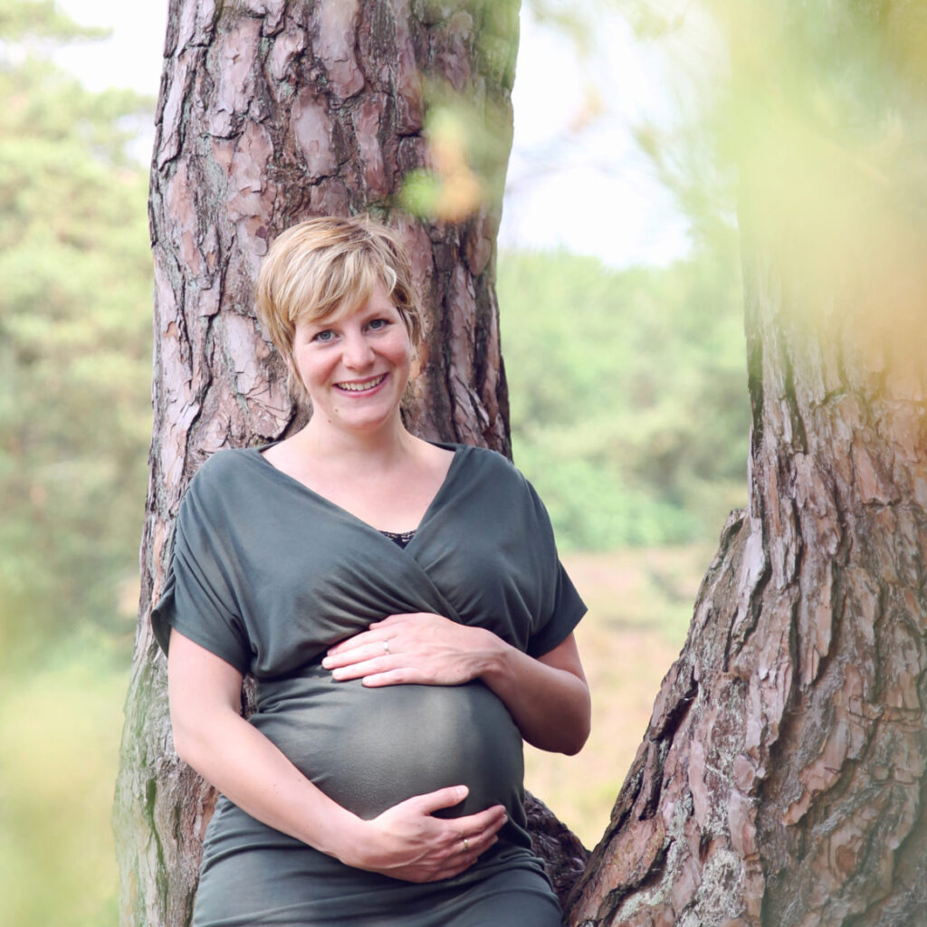 Zwangere vrouw leunt tegen een boom in het bos