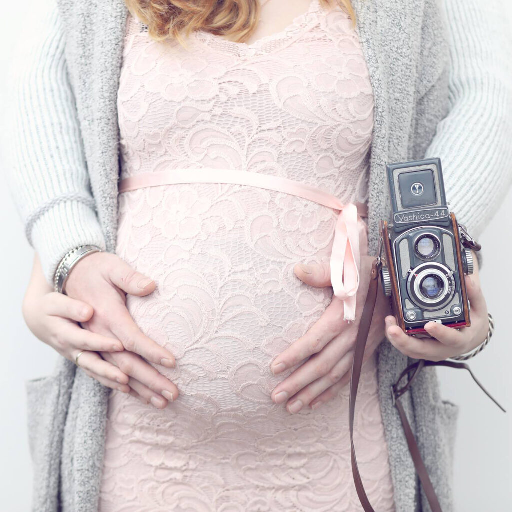 Zwangere buik in roze kanten jurk met een vintage camera