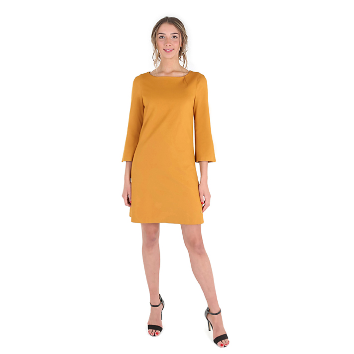Model in okergele jurk tegen een witte achtergrond, kledingfoto voor een webshop