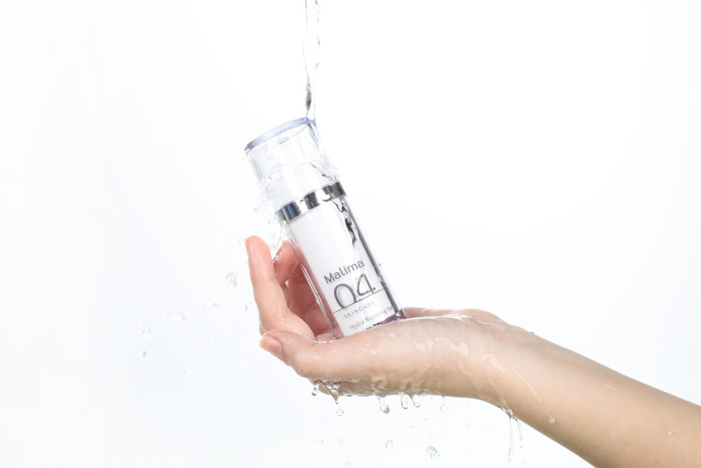 Hand vangt een flesje serum met opspattend water, productfoto