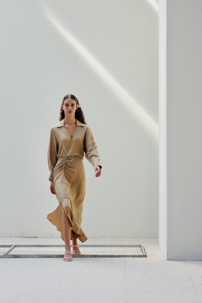 Model in beige outfit loopt over een lichte catwalk