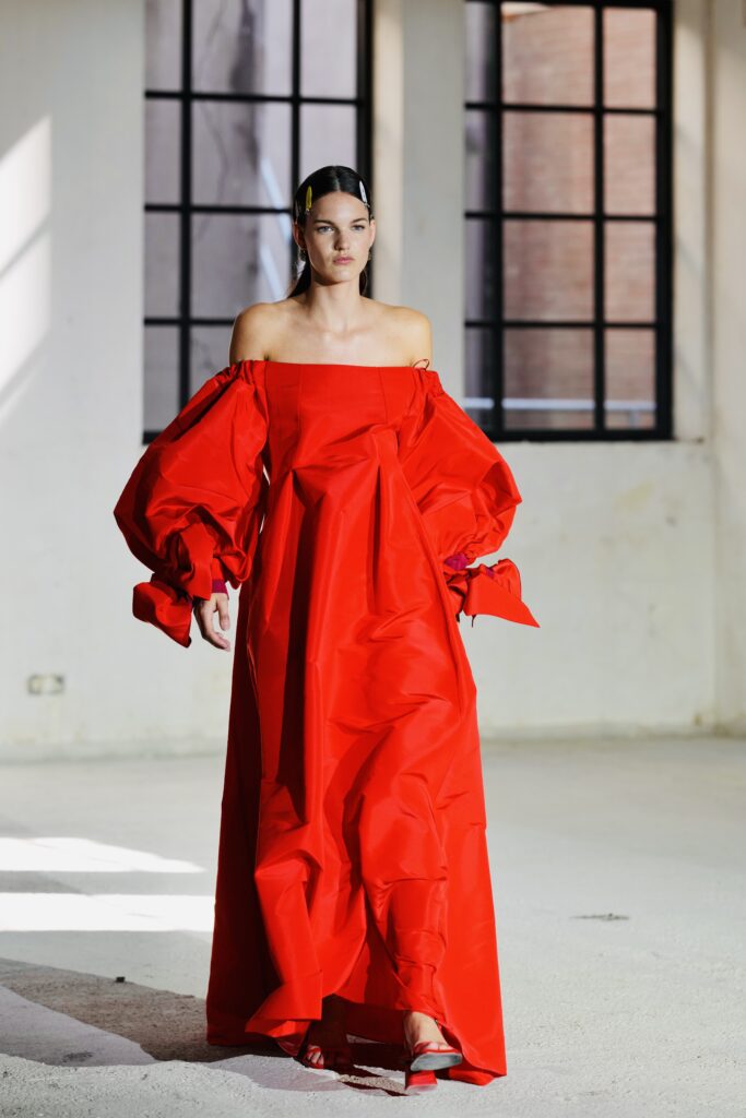 Model in rode jurk met grote mouwen in een industriële hal, modefotografie