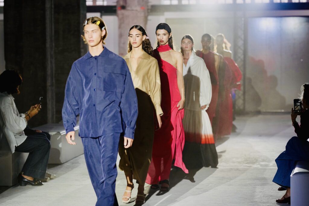 Modellen in kleurrijke outfits lopen achter elkaar over de catwalk