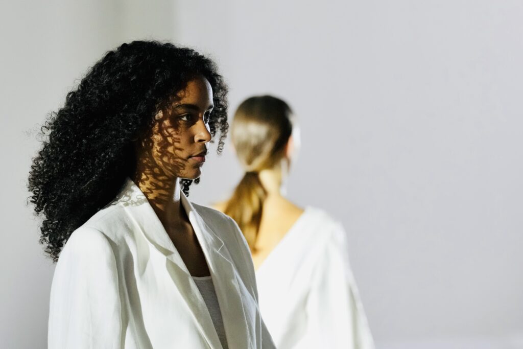 Model met krullen in wit jasje tijdens een modeshow