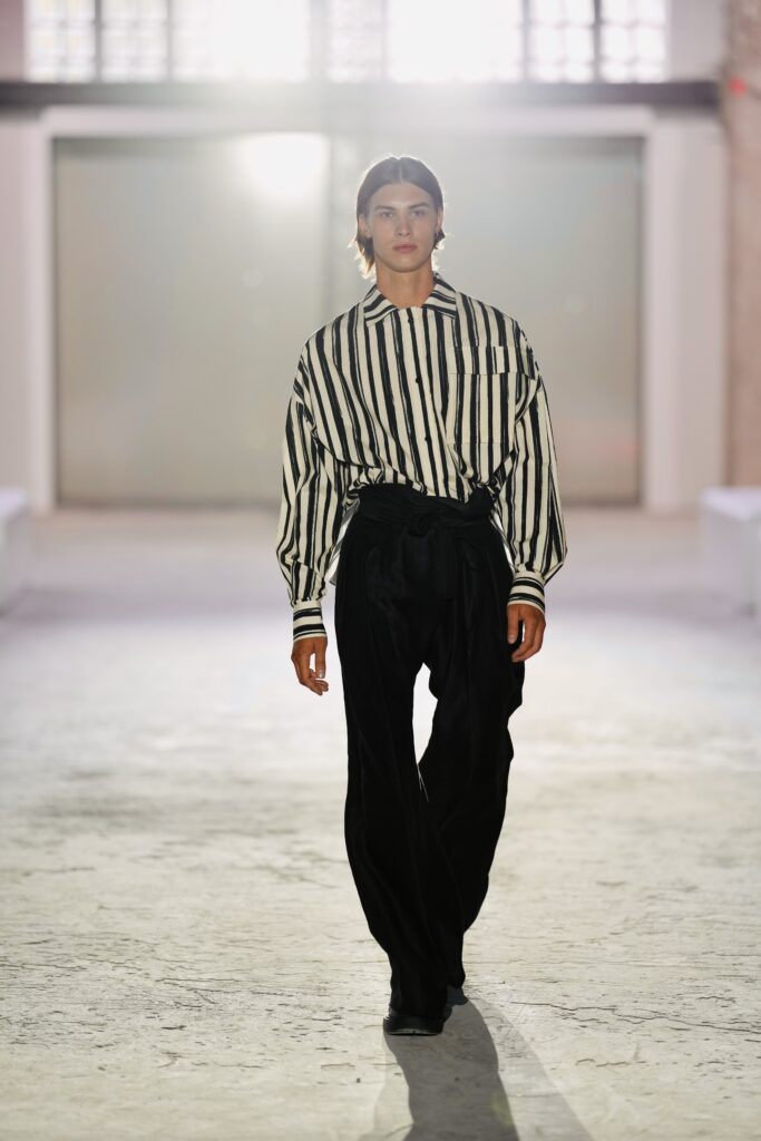 Model in gestreepte blouse en zwarte broek op de catwalk