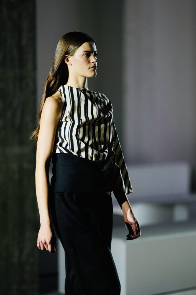 Model in zwart-wit gestreepte blouse en zwarte broek, modeshow
