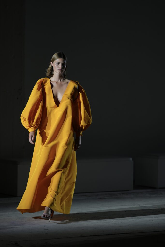 Model in gele jurk met pofmouwen tegen een donkere achtergrond