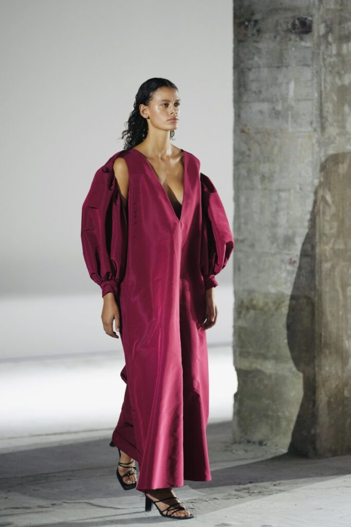 Model in fuchsia jurk met pofmouwen op de catwalk