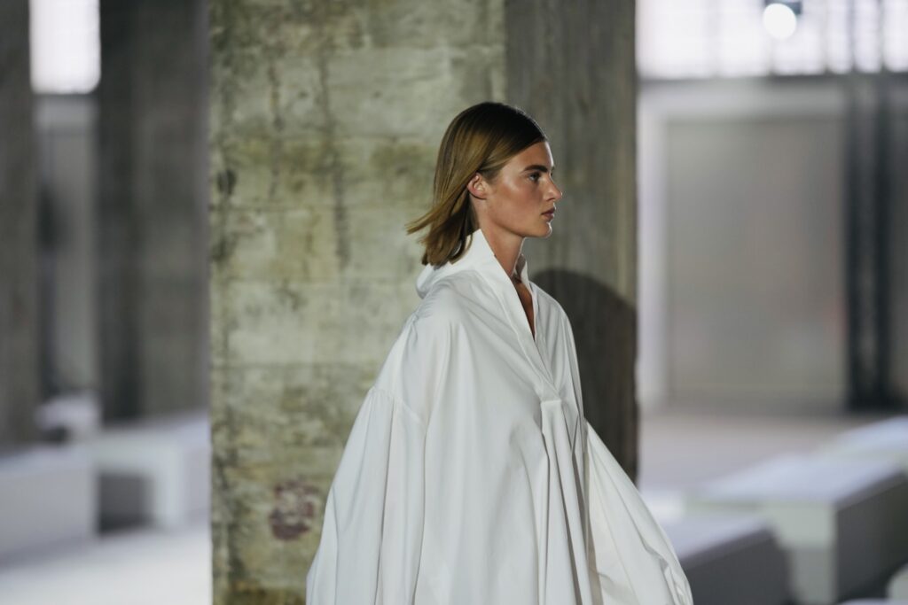 Model in witte cape bij een betonnen pilaar, modefotografie