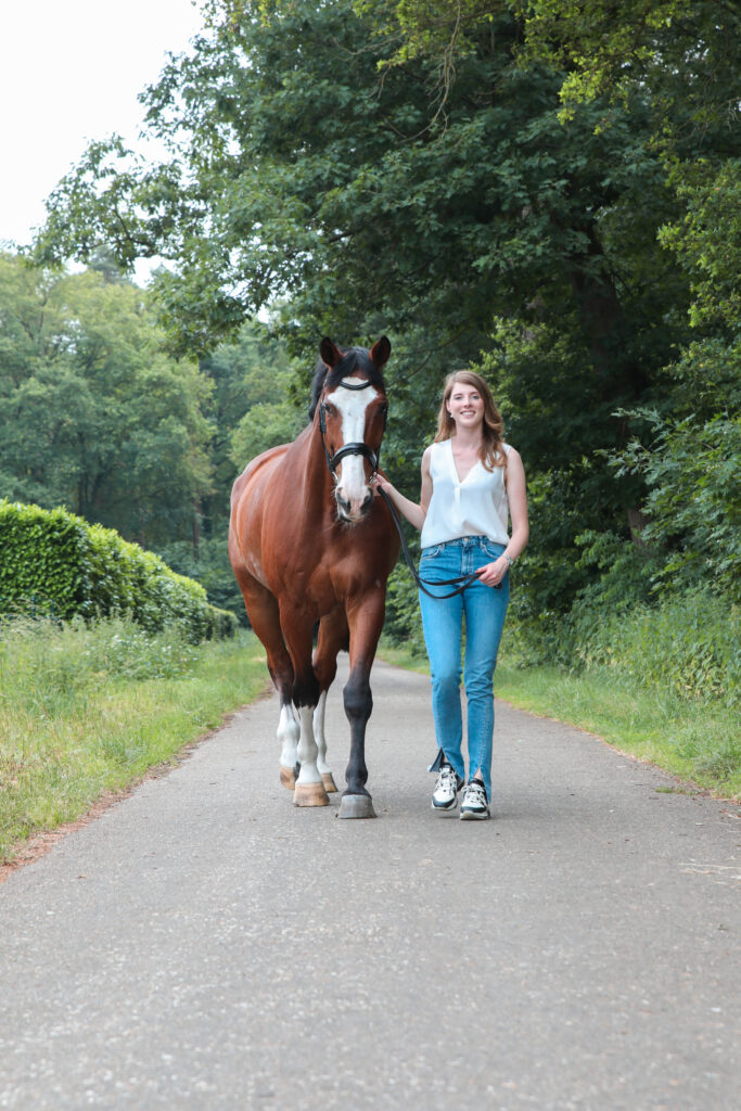 Vrouw met haar paard op een landweg tussen de bomen, paardenshoot