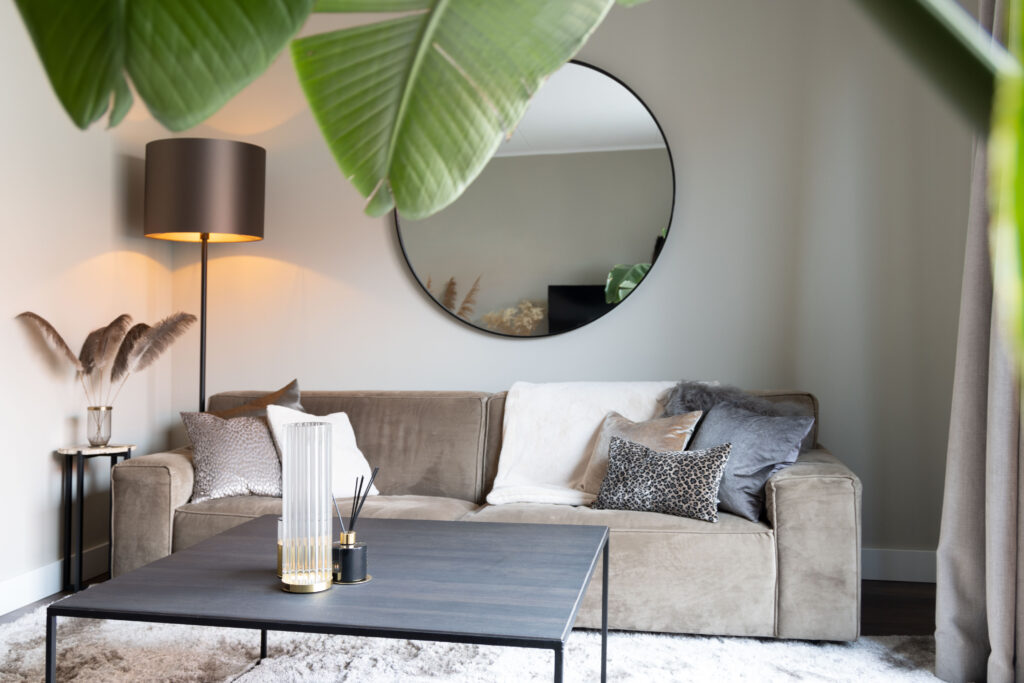 Woonkamer met ronde spiegel, bananenplant en grijze bank