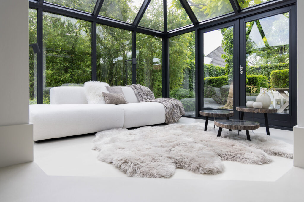 Glazen serre met witte loungebank en schapenvacht