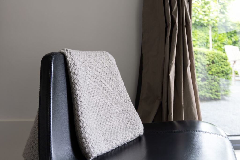 Plaid over een zwarte stoel bij het raam, sfeerdetail interieur
