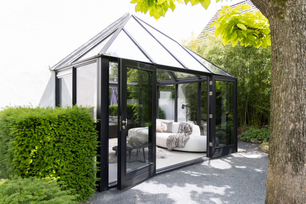 Glazen tuinkamer met loungebank in een groene tuin, vastgoedfotografie