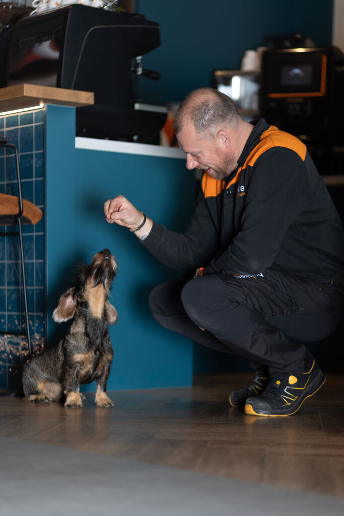 Man geeft zijn teckel een snoepje in de keuken, hondenfotografie thuis