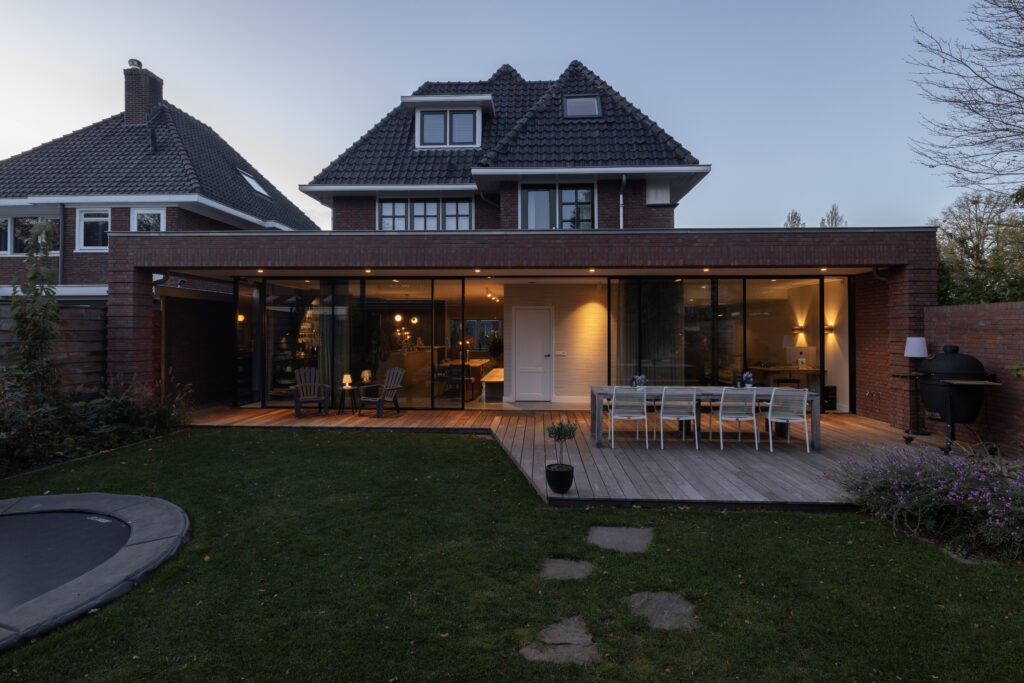 Achtergevel van een villa met verlichte aanbouw bij schemering