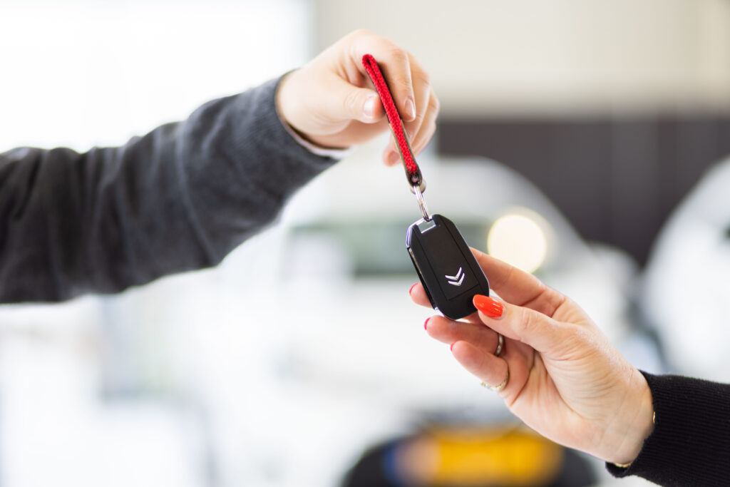 Hand geeft een autosleutel met rood keykoord over, productfoto