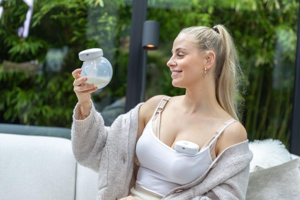 Vrouw bekijkt een draagbare borstkolf in een lichte woonkamer, lifestyle productfoto