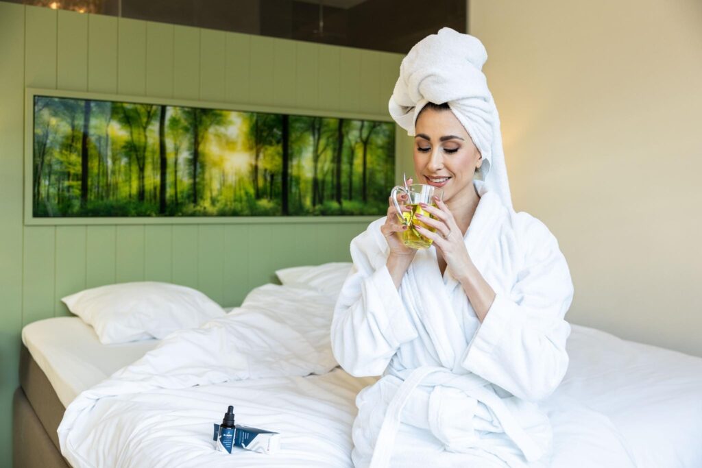 Vrouw in badjas met handdoek op bed drinkt thee, lifestyle productfoto voor een hotel
