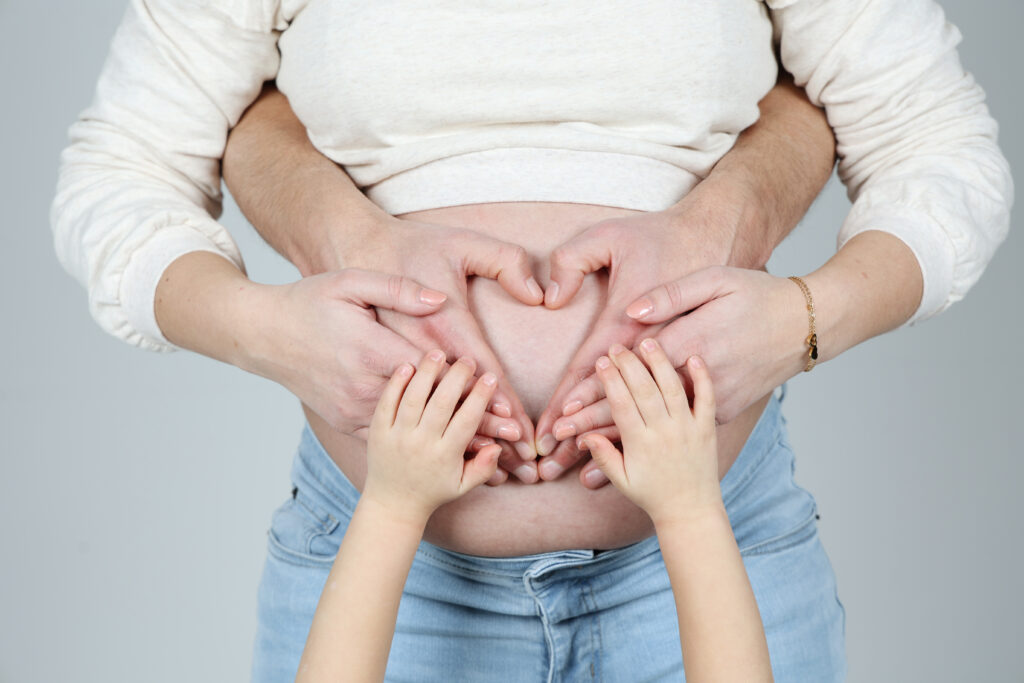 Kinderhandjes vormen een hart op de zwangere buik van mama